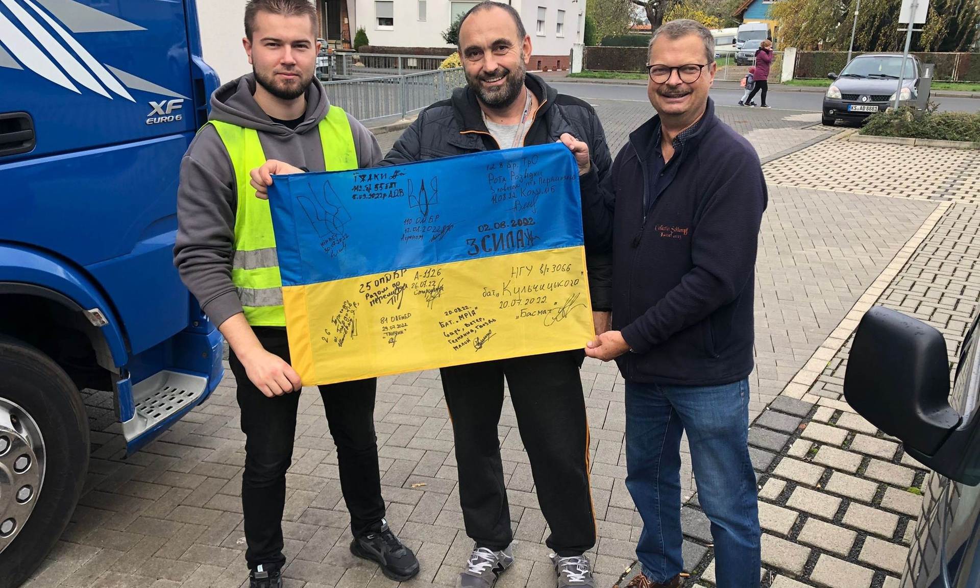 Drei Männer halten ein Plakat in den ukrainischen Farben hoch