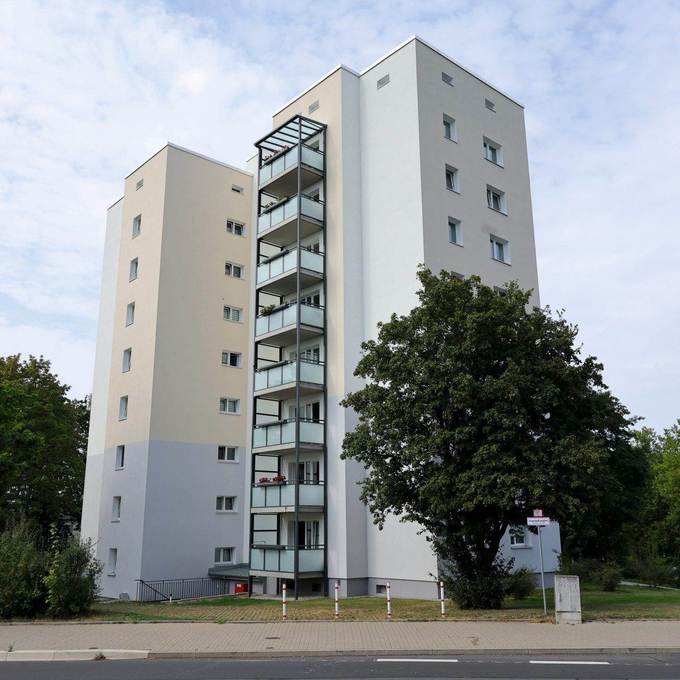 Blick auf ein modernisiertes Hochhaus, links und rechts davon stehen Bäume