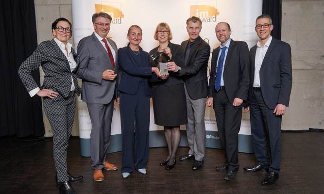 Genannte Personen, mit dem im-Award in Händen, vor einer Wand stehend.