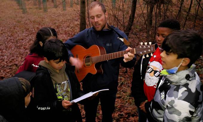 In der Mitte von Kindern spielt ein junger Mann Gitarre und singt.