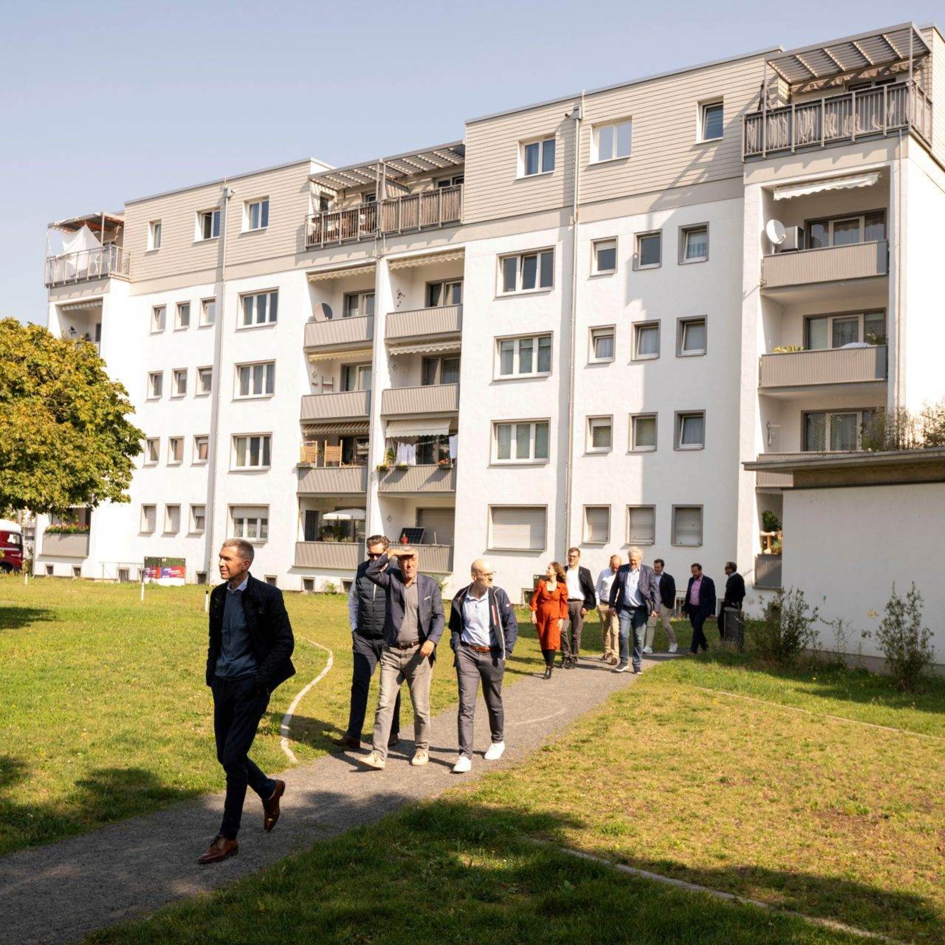 Eine Gruppe von Männern läuft über eine Wiese, im Hintergrund ein Mehrfamilienhaus