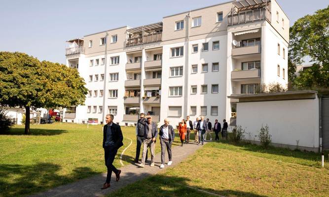 Eine Gruppe von Männern läuft über eine Wiese, im Hintergrund ein Mehrfamilienhaus