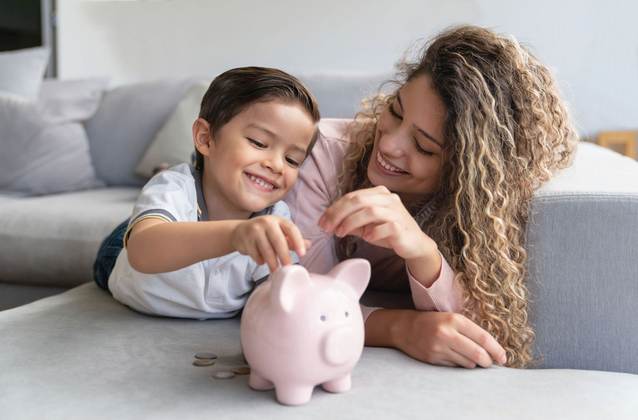 Frau und Kind liegen auf dem Sofa und werfen Münzen in ein Sparschwein.