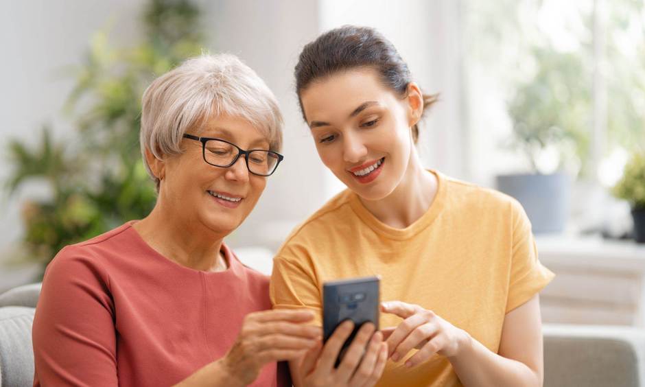 Ältere Frau und jüngere Frau schauen gemeinsam auf ein Handy.