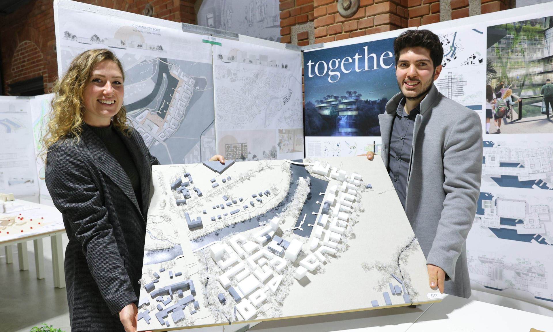 Melissa Krug und Necati Karalar halten ein Plakat mit ihrem Entwurf in der Hand