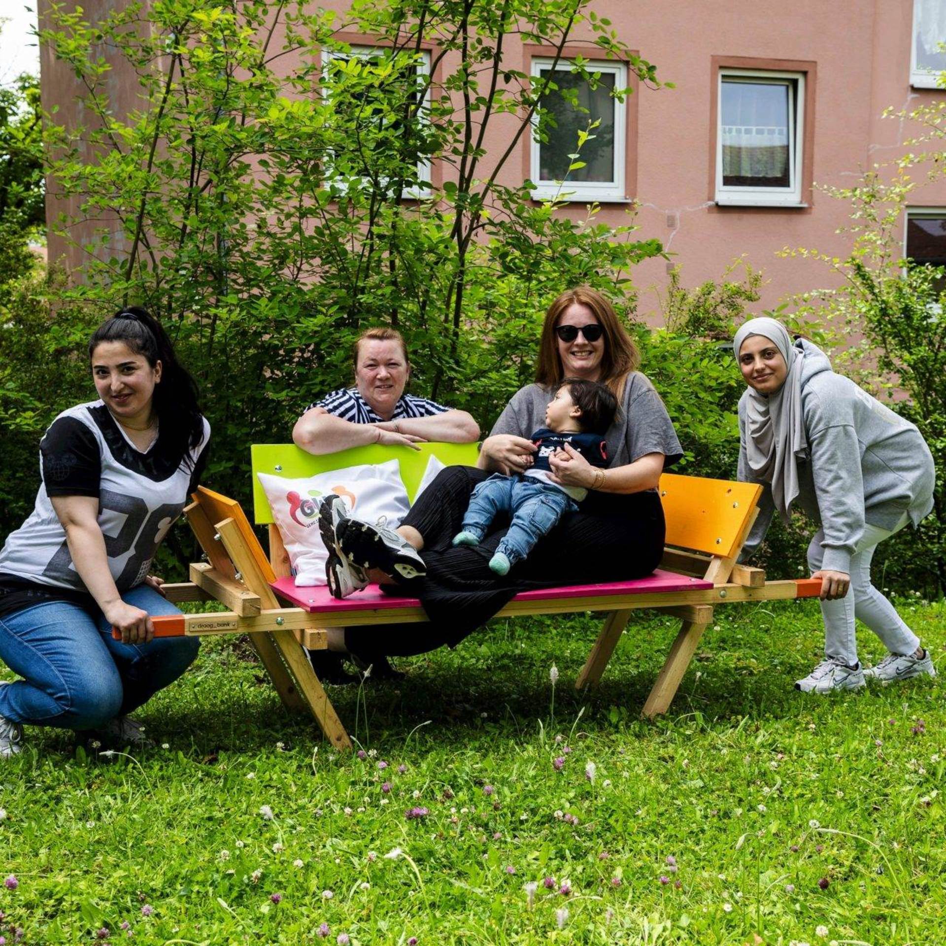 Eine Frau und ein kleines Kind sitzen auf einer bunt bemalten Bank, drei weitere Frauen hocken links, rechts und hinter der Bank