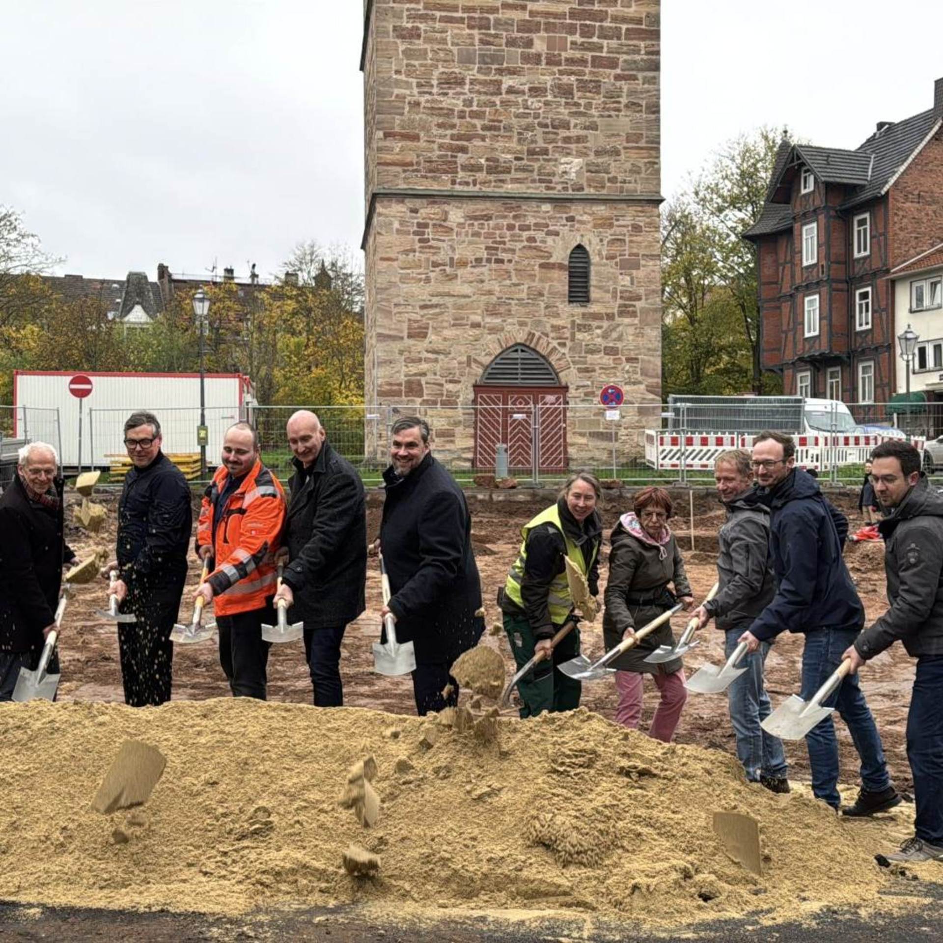 Elf Menschen mit Spaten in der Hand hinter einem Sandhaufen, hinter ihnen ein alter Turm