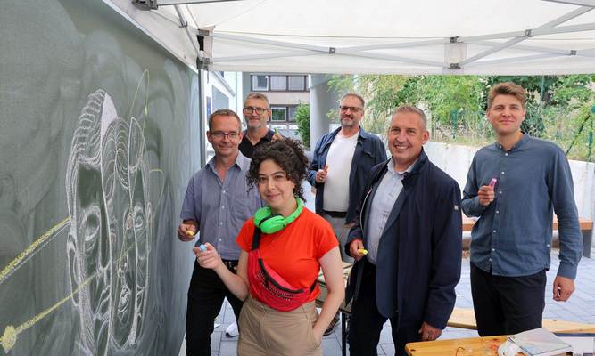 Gruppenfoto vor der Tafel: Künstlerin Aliaa Abou Khaddour sowie (v. li.) Matthias Otto (Leiter Servicecenter Kassel), Frank Jungermann (Kundenmanager), Friedemann Bunge (Projektleiter Neubau), Sascha Holstein (Leiter Regionalcenter Kassel) und Alexander Hauschild (Projektleiter Soziale Quartiersentwicklung).