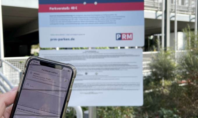 Handy mit geöffneter Park-App vor Schild mit Parkhaus-Infos