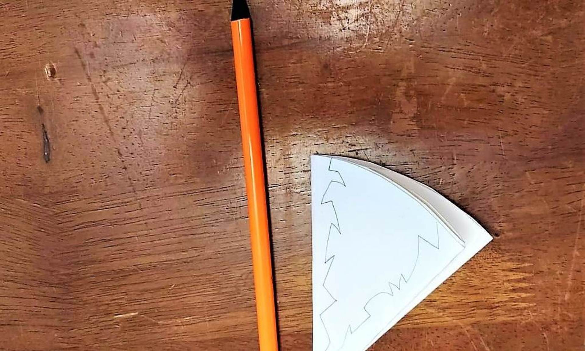 Ein Stift und ein gefaltetes Stück Papier liegen auf dem Tisch. Auf dem Papier ist ein Umriss aufgezeichnet.