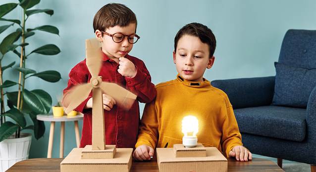 Zwei Jungen erzeugen mit einem kleinen Windrad Strom für eine Glühbirne.
