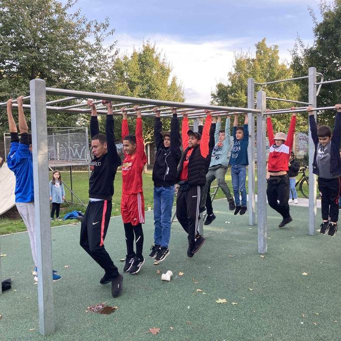 Mehrere junge Menschen hangeln sich an einem Fitnessgerät entlang