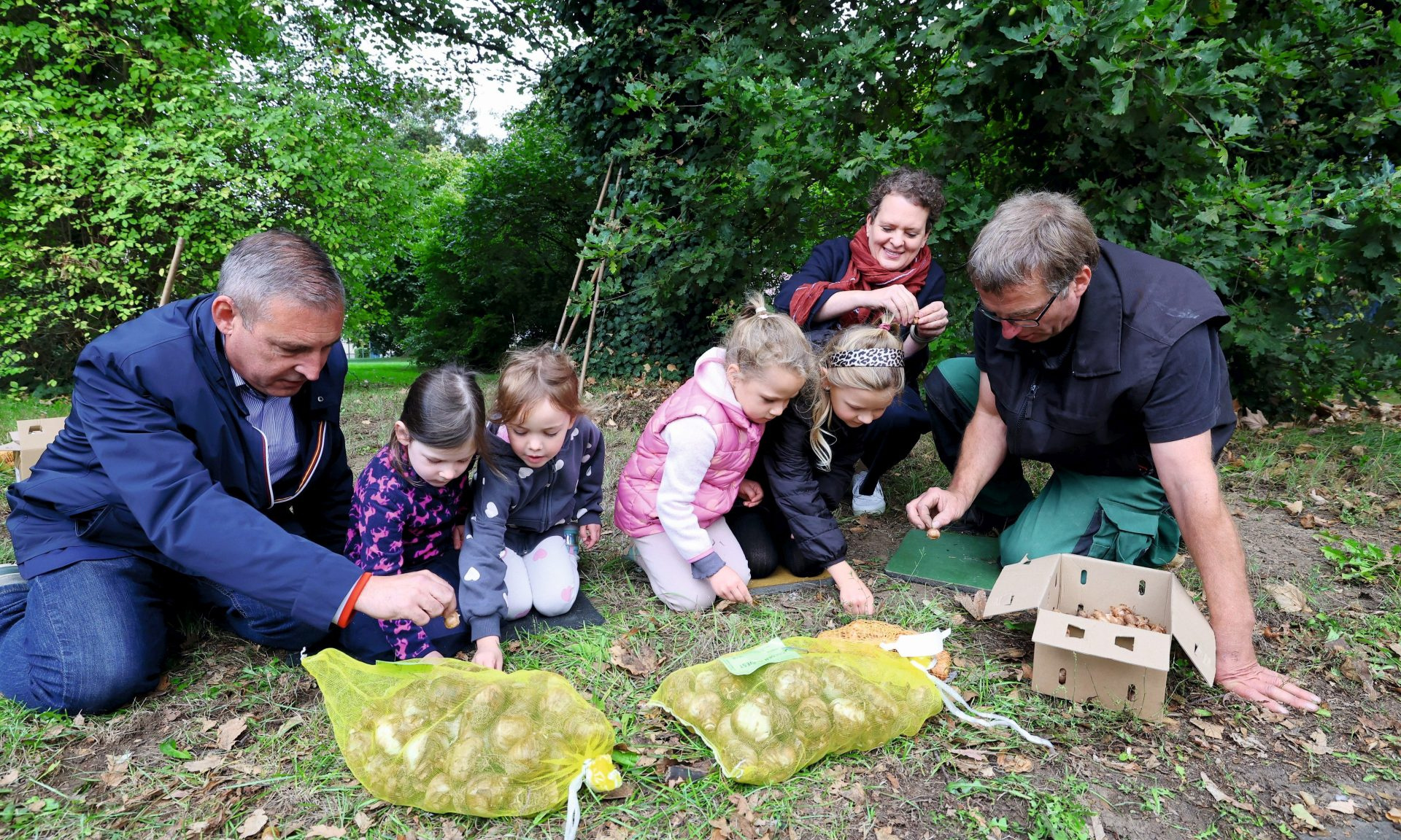 Sascha Holstein (li., Leiter NHW-Regionalcenter Kassel), Susanne Hardekopf (NHW, Planerin Freiflächenservice) sowie Jens Steuber vom GaLaMa-Projekt helfen Kindern beim Einpflanzen der Blumenzwiebeln..