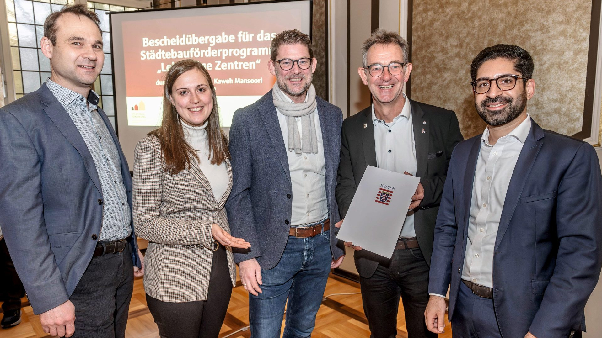 Gruppenfoto: Staatsminister Kaweh Mansoori (re.) hat einen Förderbescheid über 3,3 Millionen Euro an Bürgermeister Christian Schönung (2.v.re.) übergeben. Die ProjektStadt – (v. li.) Christian Schwarzer, Laura Pfisterer und Gregor Voss – unterstützt beim Fördermittelmanagement. 