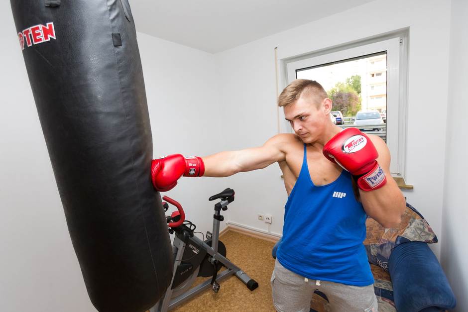 Ein junger Mann boxt auf einen Boxsack. Er hat Boxhandschuhe an.