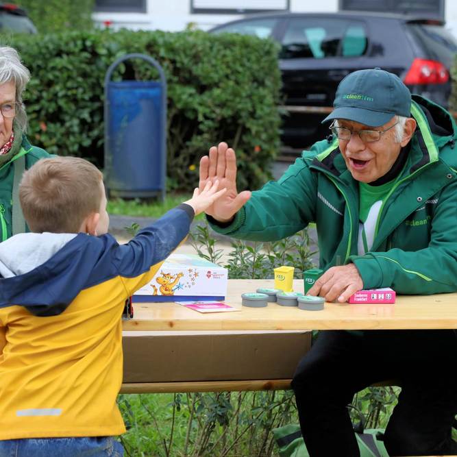 Ein älterer Mann und eine ältere Dame sitzen hinter einem Holztisch, der Mann gibt einem Jungen High Five