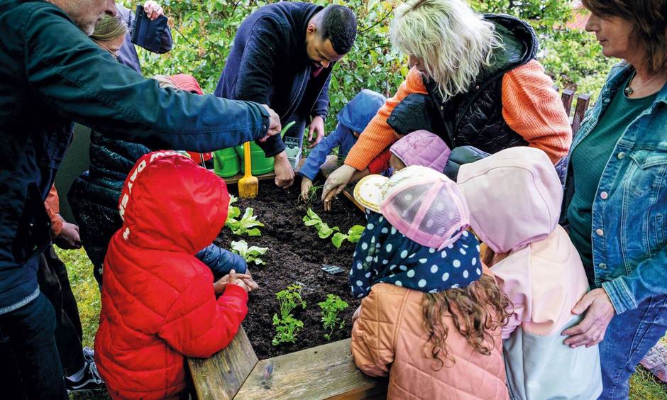 Erwachsene und Kinder pflanzen einige Pflanzen in ein Hochbeet ein.