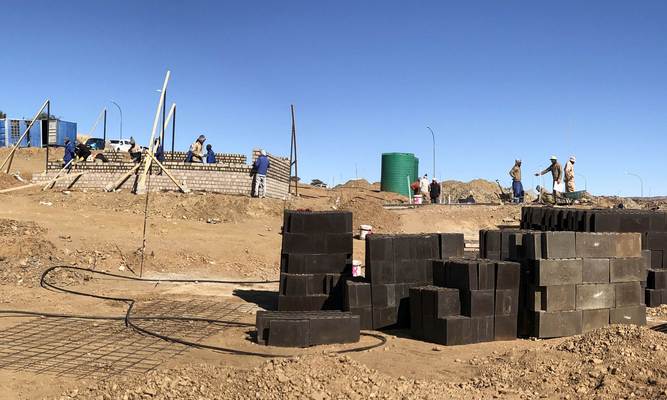 Bauarbeiter bauen zwei Häuser, im Vordergrund Mauersteine