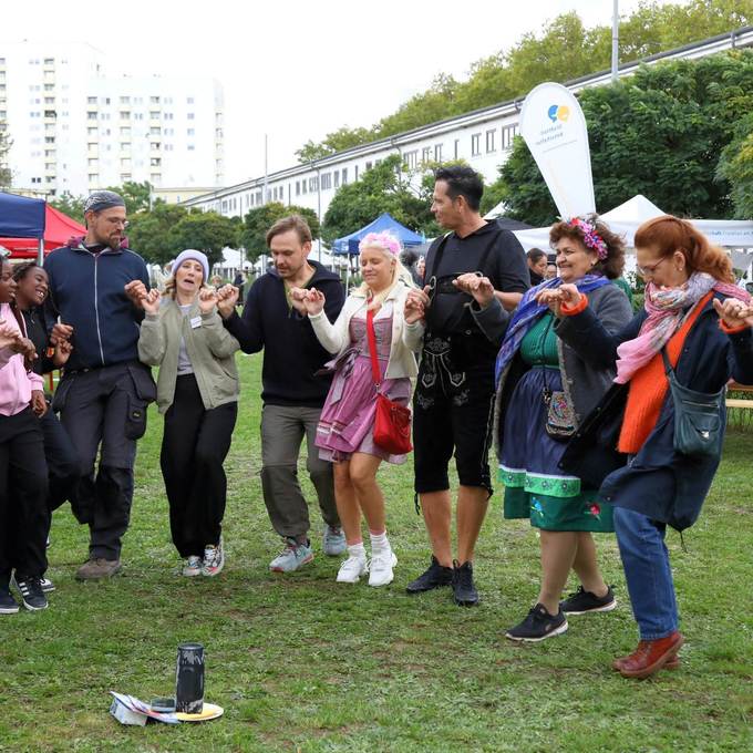 Mehrere Menschen tanzen  in einem Halbkreis, jeder hält seine Nachbarn an den Händen