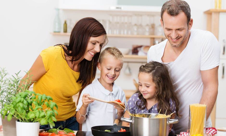 Mutter, Vater, Sohn und Tochter stehen zusammen am Herd und probieren das Essen.