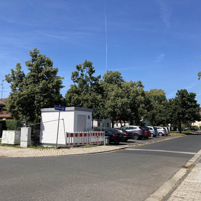 Blick auf einen Grünstreifen mit Baucontainer und parkenden Autos, im Vordergrund Straße