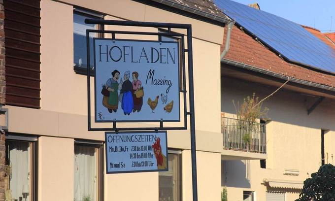 Schild mit Aufschrift "Hofladen" und Öffnungszeiten vor Mehrfamilienhaus