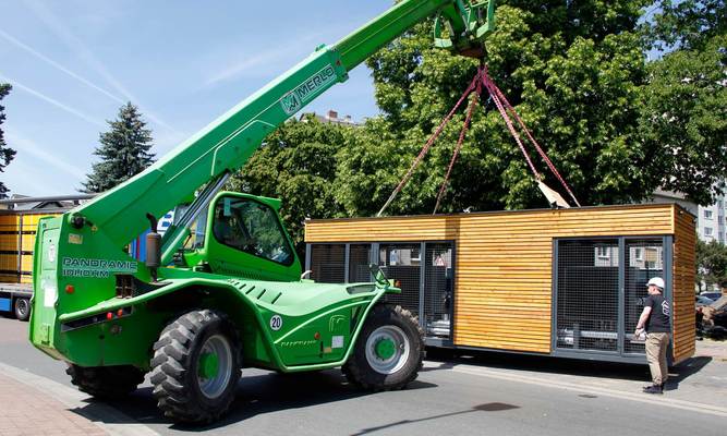 Ein grüner Teleskoplader hebt Energiemodul mit je sechs Luft-Wasser-Wärmepumpe an.