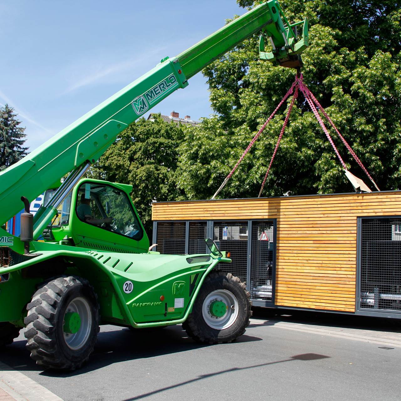 Ein grüner Teleskoplader hebt Energiemodul mit je sechs Luft-Wasser-Wärmepumpe an.