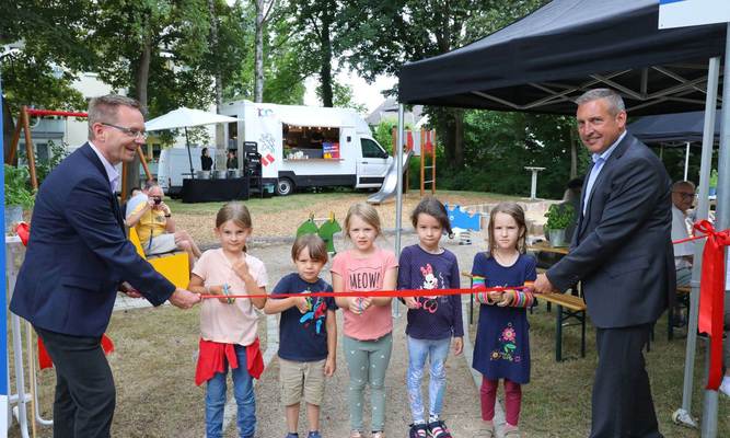 Zwei Männer und fünf Kinder schneiden ein Band durch