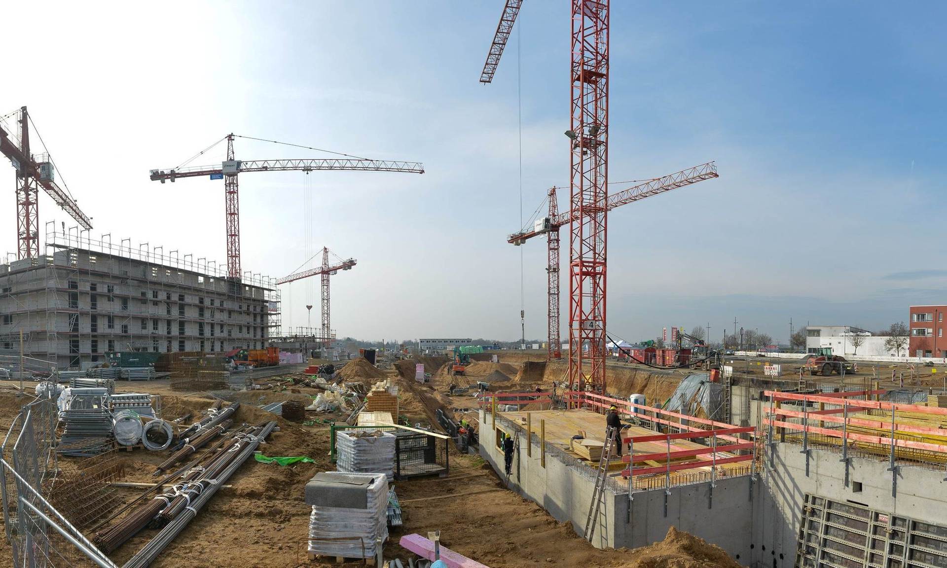 Überblicksfoto über die Baustelle mit Baugrube, Kränen sowie einem weiter fortgeschrittenen Rohbau