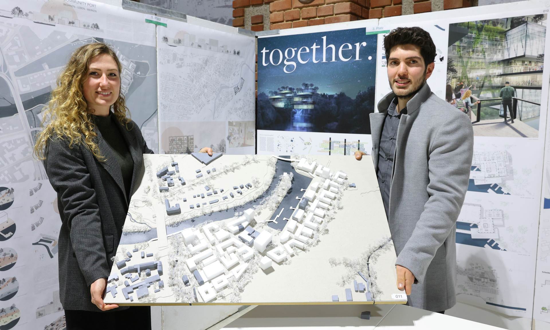 Eine junge Frau und ein junger Mann präsentieren ein architektonisches Modell für die Gestaltung eines Quartiers.