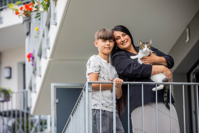 Frau mit Katze auf dem Arm und Junge stehen auf einem Balkon.