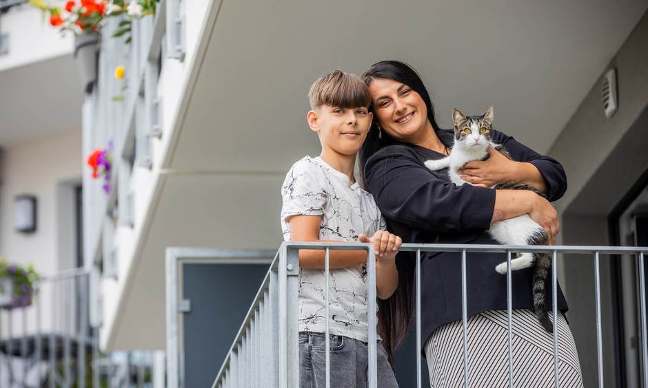 Frau mit Katze auf dem Arm und Junge stehen auf einem Balkon.