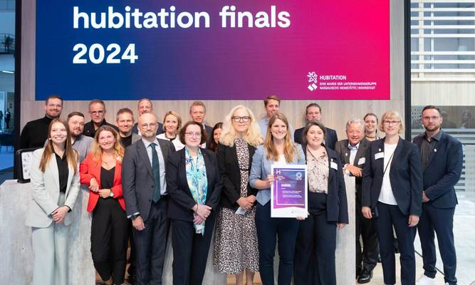 Gruppenfoto mit vielen gut gelaunten und lachenden Menschen, darüber ein Screen mit der Aufschrift "hubitation finals 2024"