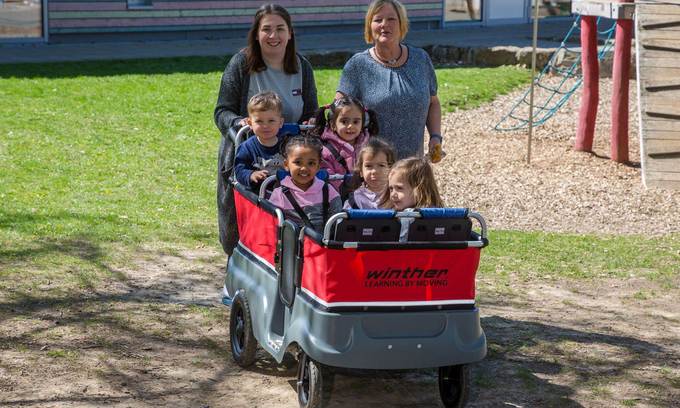 Zwei Frauen schieben einen Wagen, in dem mehrere Kinder sitzen